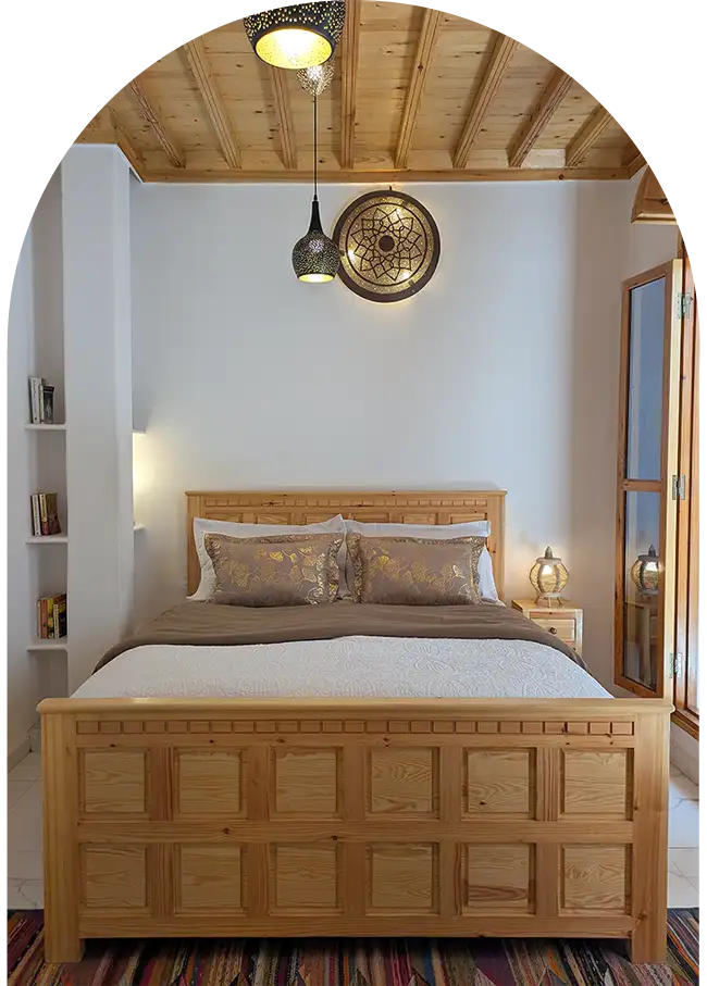 Suite familiale avec son lit sculpté, son plafond en bois blond et ses grandes portes fenêtres donnant sur le patio du riad